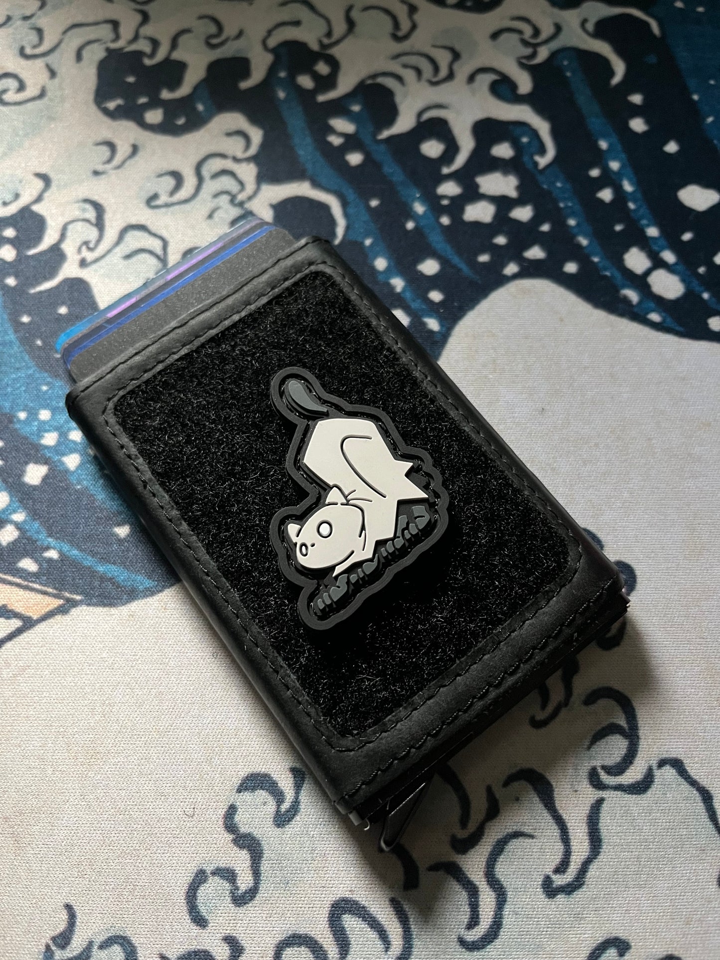 Crouching Ghost Cat RE ranger eye patch of a crouching cartoon cat wearing a white ghost costume on a velcro wallet with a Great Wave background.