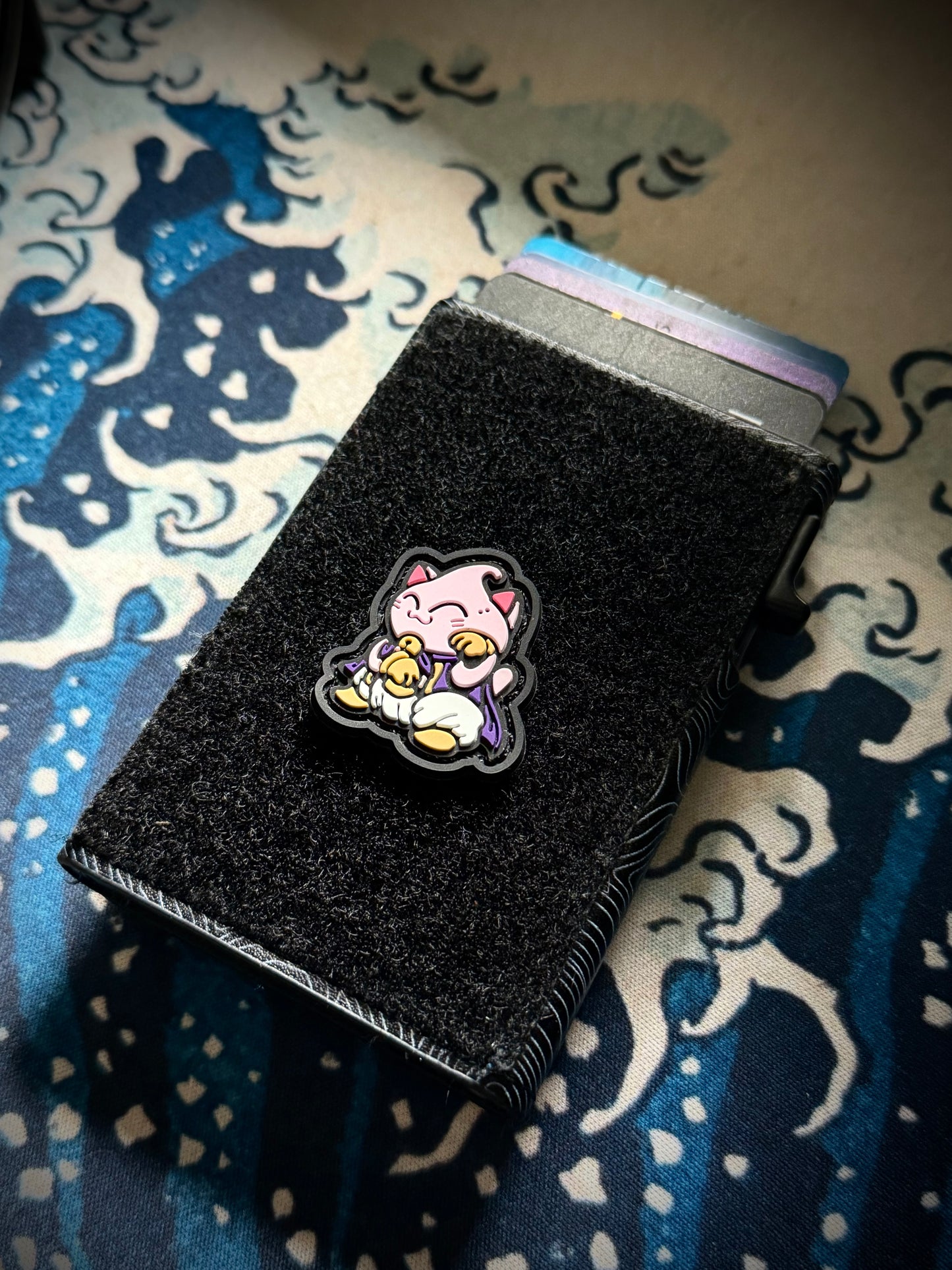 Majin Neko RE colorful pink cartoon character in a lucky cat maneki neko pose on a velcro wallet with a Great Wave background.
