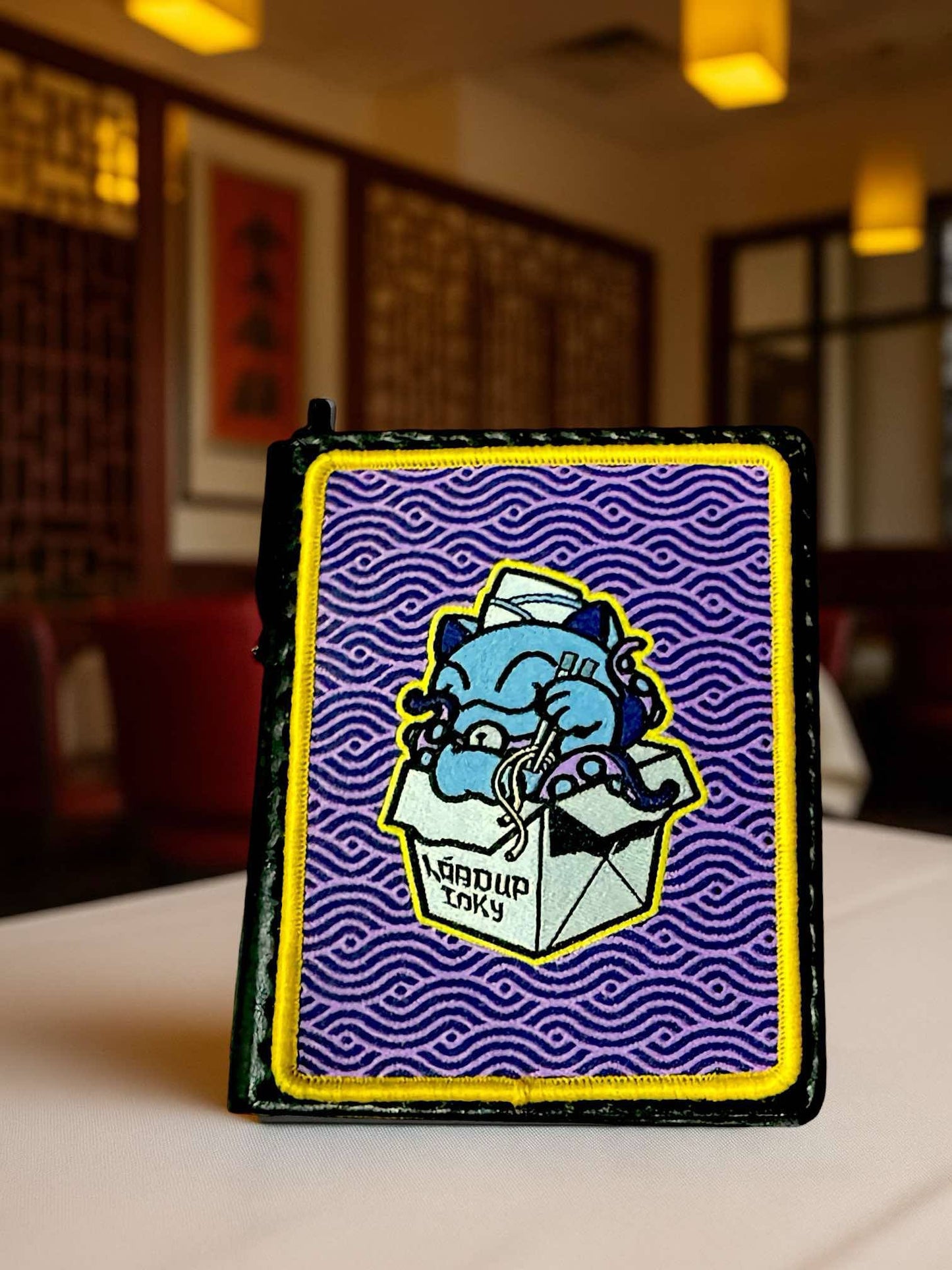 Tentekko Patch Set woven nylon patch of a blue cat in a takeout box with a purple background in a restaurant setting.