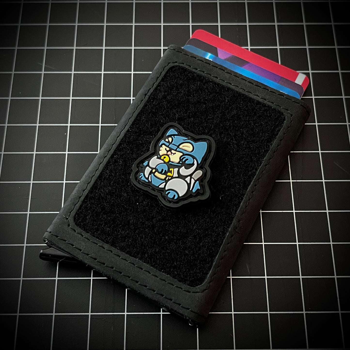 Batman Neko RE PVC ranger eye morale patch of a superhero wearing a mask in a lucky cat maneki-neko pose on a velcro wallet and grid background.