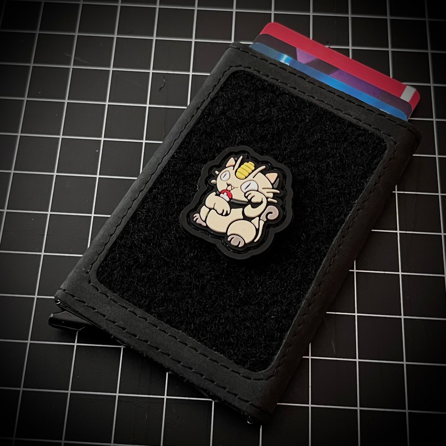 Meowth Neko RE PVC ranger eye morale patch of a white cat with coin forehead sitting in a lucky cat maneki-neko pose on a velcro wallet and grid background.