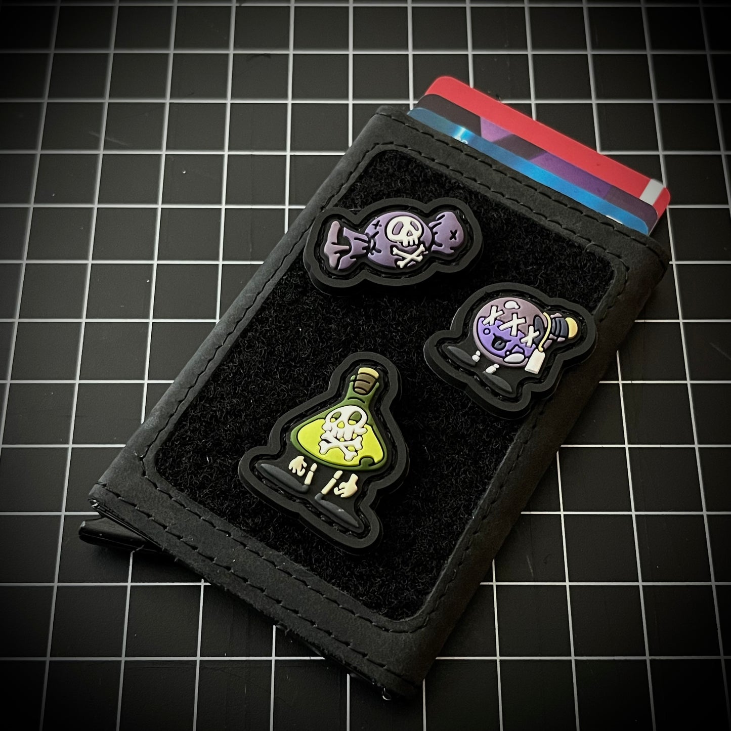Poison Beaker RE, Poison Candy RE, and Poison Flask RE on a velcro wallet and a grid background.