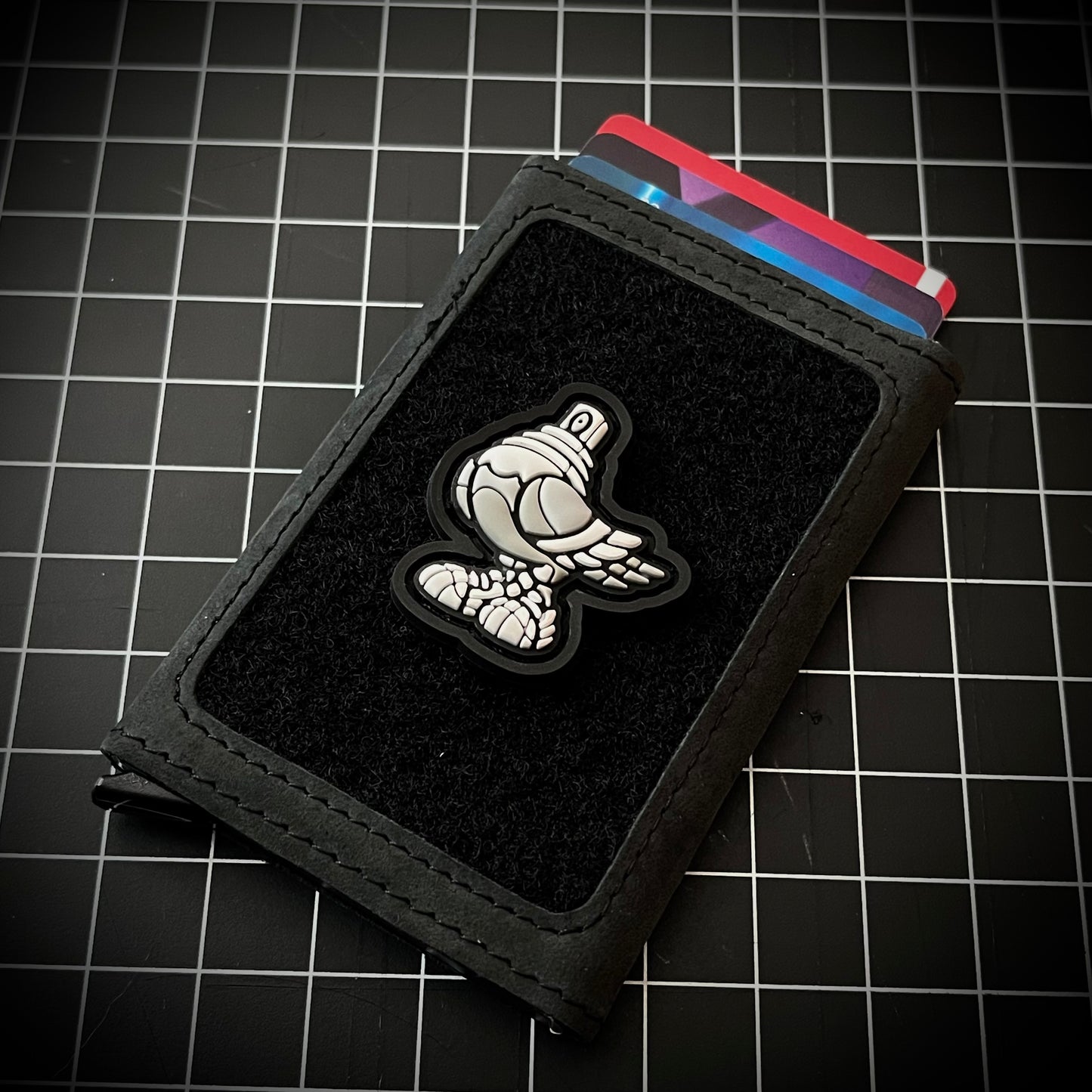 Spraygeon RE - Grayscale PVC ranger eye morale patch of a grayscale colored pigeon with a spray paint cap head wearing tennis shoes on a velcro wallet and a grid background.