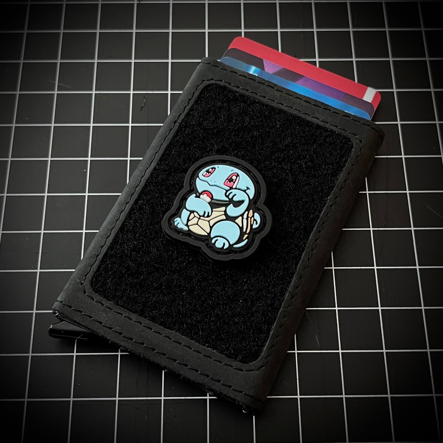 Squirtle Neko RE PVC ranger eye morale patch of a blue turtle character sitting in a lucky cat maneki-neko pose on a velcro wallet and a grid background.