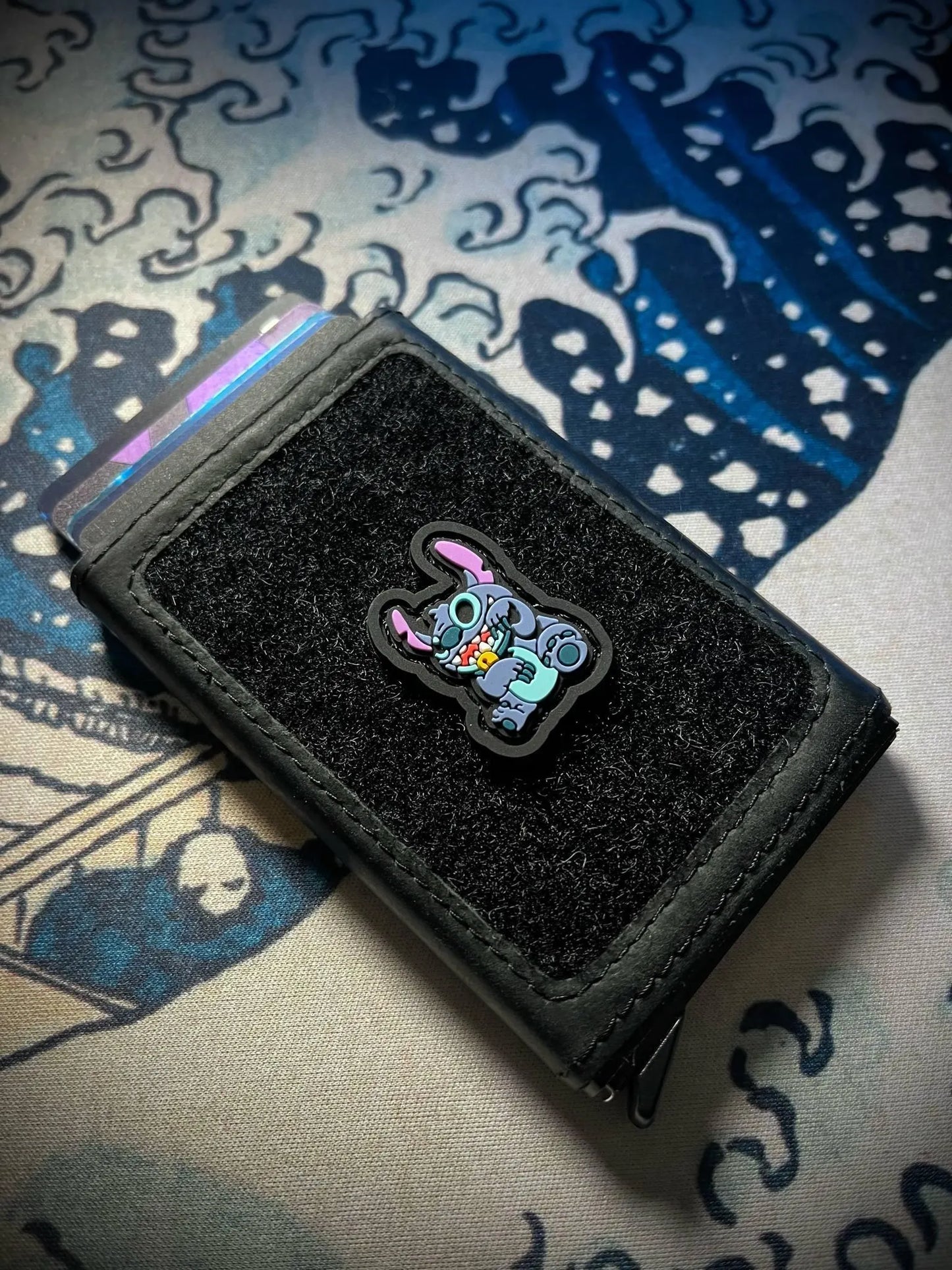 Stitch Neko RE ranger eye morale patch of a cute blue alien cartoon sitting in a lucky cat maneko pose on a velcro wallet with a Great Wave background.