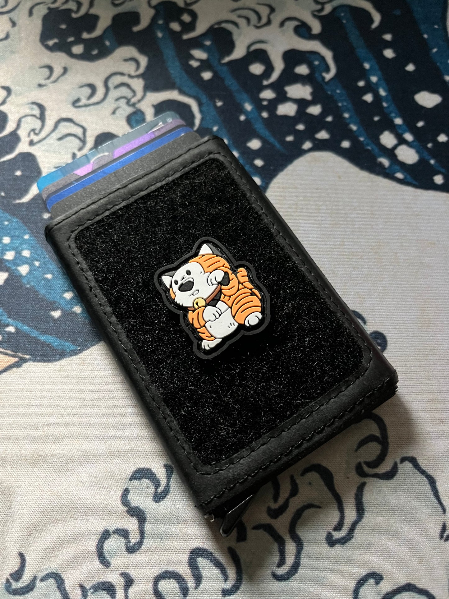 Comic Tiger Neko RE ranger eye patch depicting a cartoon tiger in a lucky cat maneki neko pose on a velcro wallet with a Great Wave background.