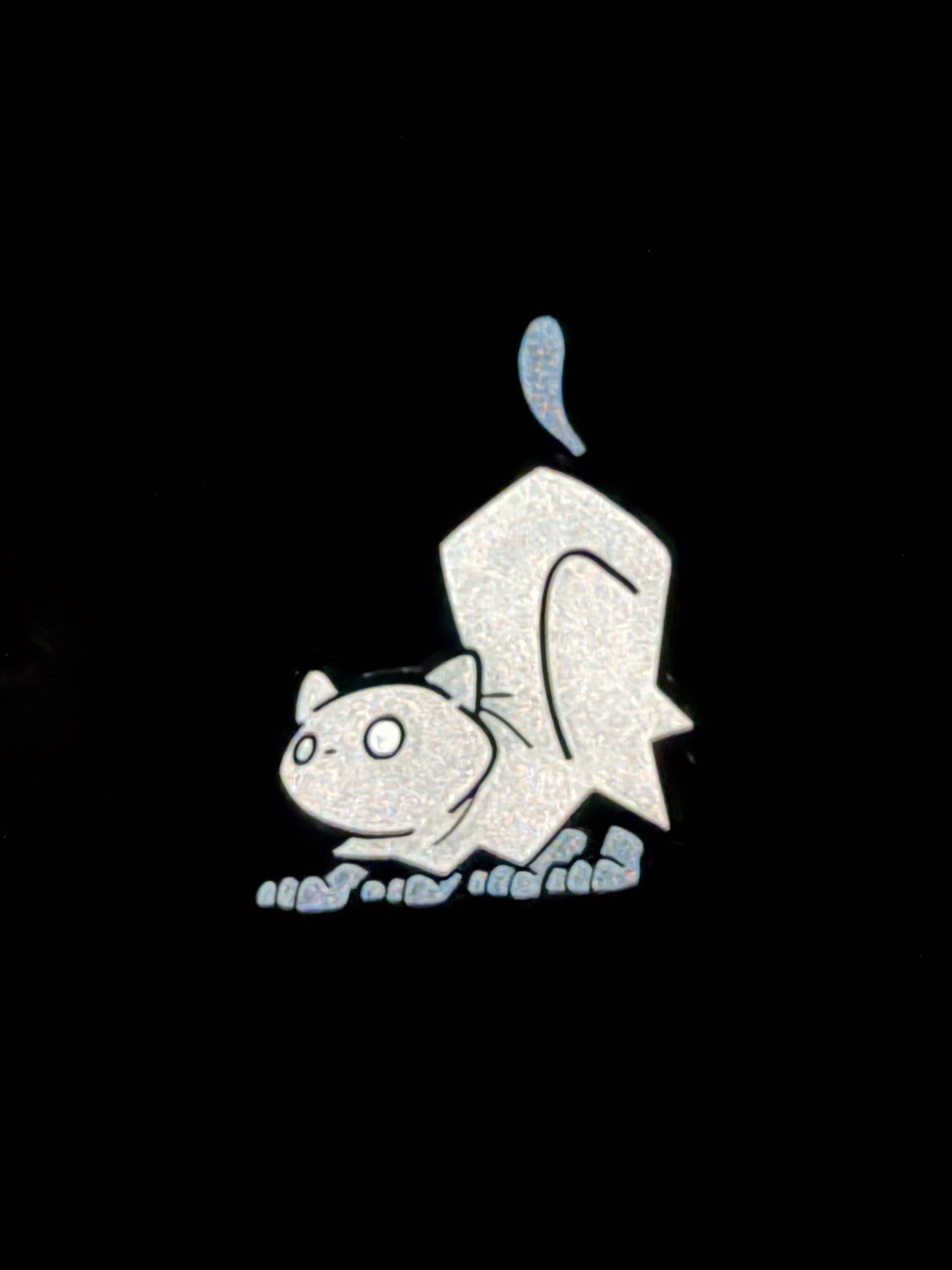 Glow in the dark photo of the enamel pin depicting a cat in a ghost outfit crouching.