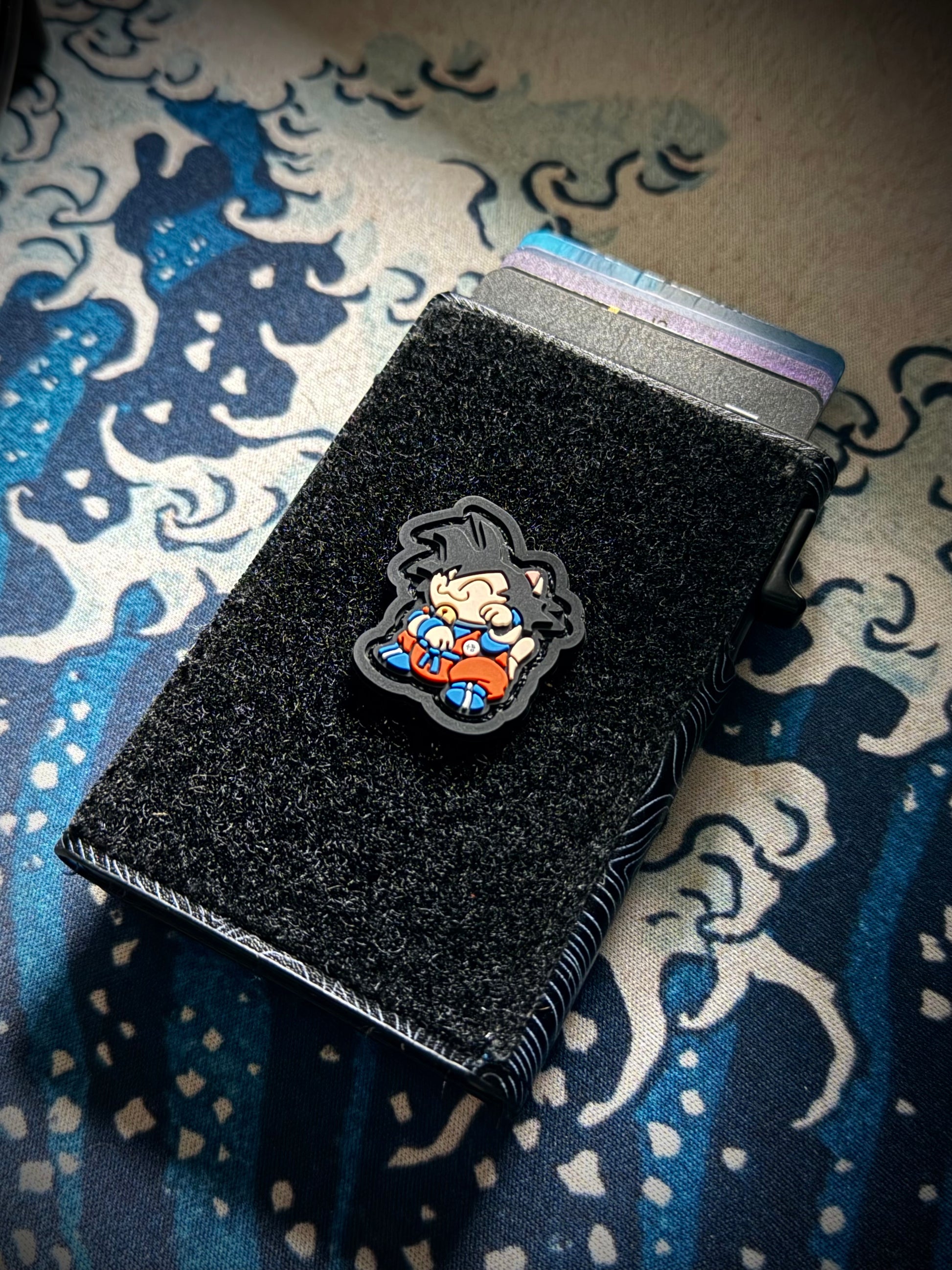 Goku Neko RE Dragon Ball velcro patch - Cartoon character with black hair and orange outfit on a black background on a velcro wallet with a great wave background