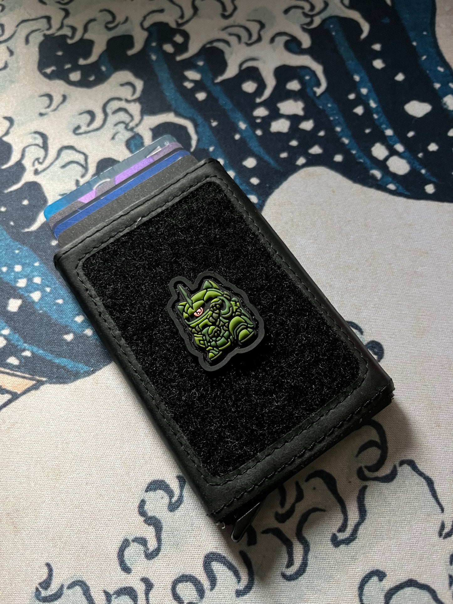 Green Zaku Neko RE ranger eye morale patch of a green mechanical lucky cat on a wallet with a Great Wave background.