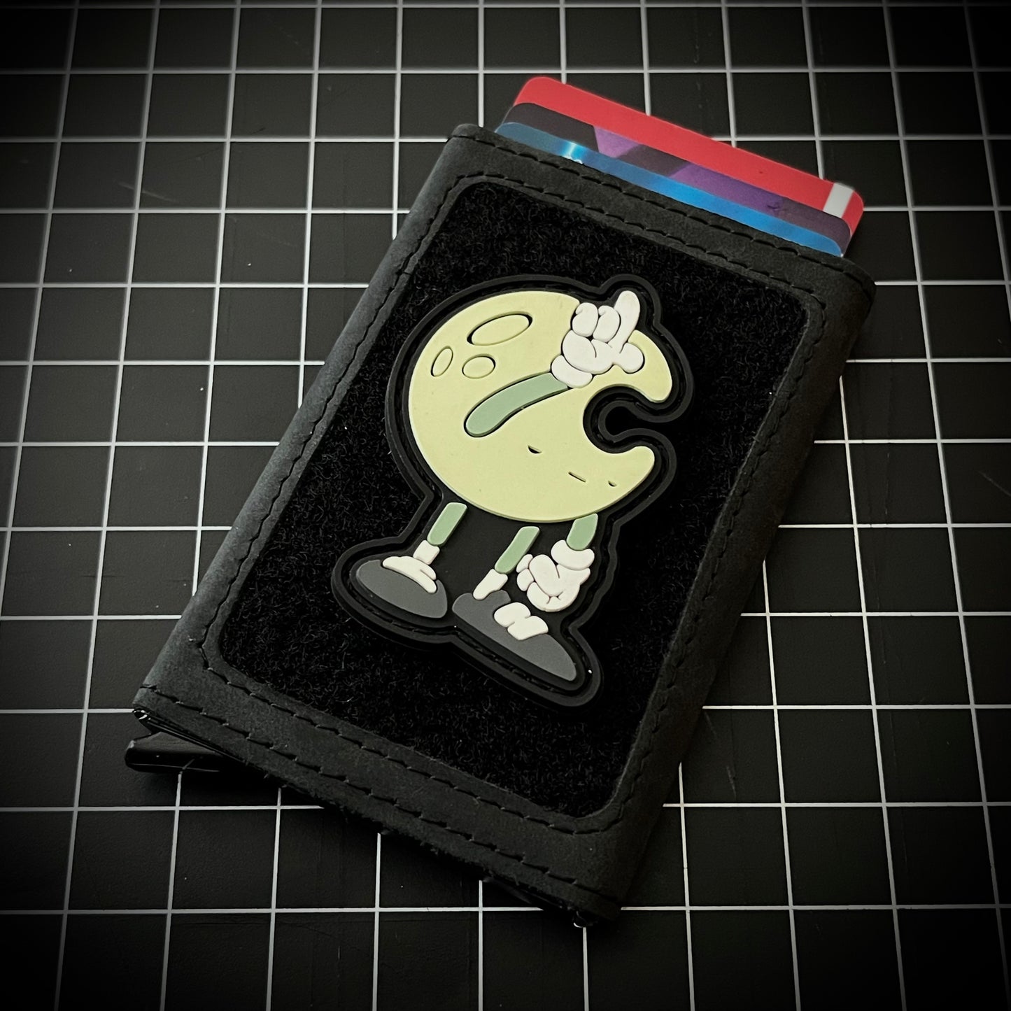 Lunar LoadUp RE PVC ranger eye morale patch featuring a cartoon moon character creating an L shape with it's hand on its forehead on a velcro wallet and grid background.
