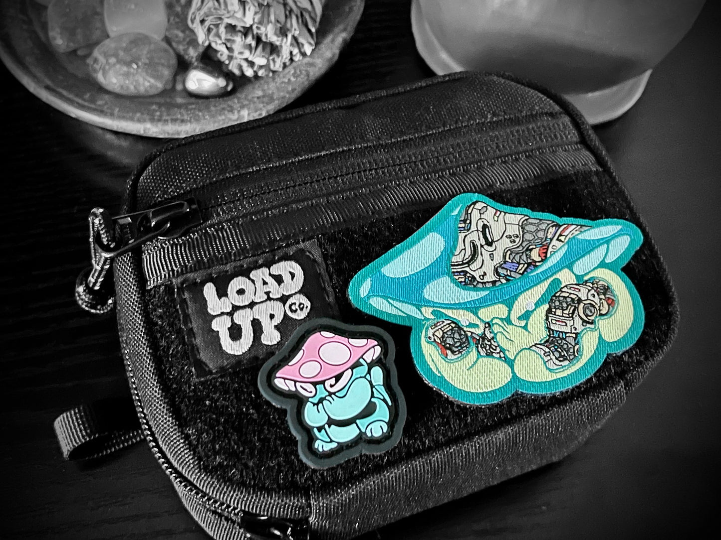 Praying Mushroom Patch Set depicting 2D PVC patch of a green mushroom character with pink and white cap in a lucky cat maneko pose and a woven nylon mechanical style green mushroom patch on a LOADUP pouch.