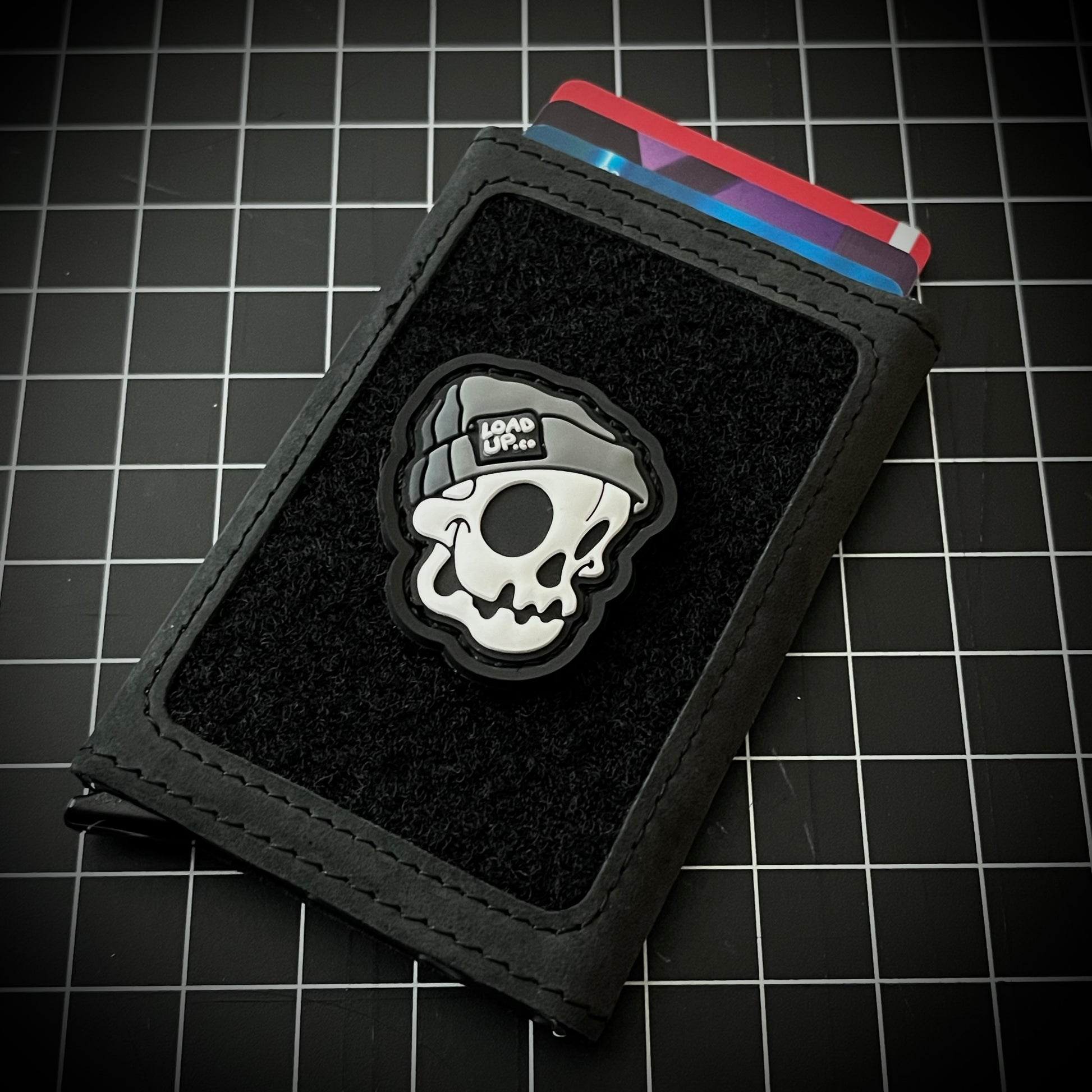 Beanie Skull RE PVC ranger eye morale patch of a skull head wearing a gray beanie with a LOADUP.co label on a velcro wallet and grid background.