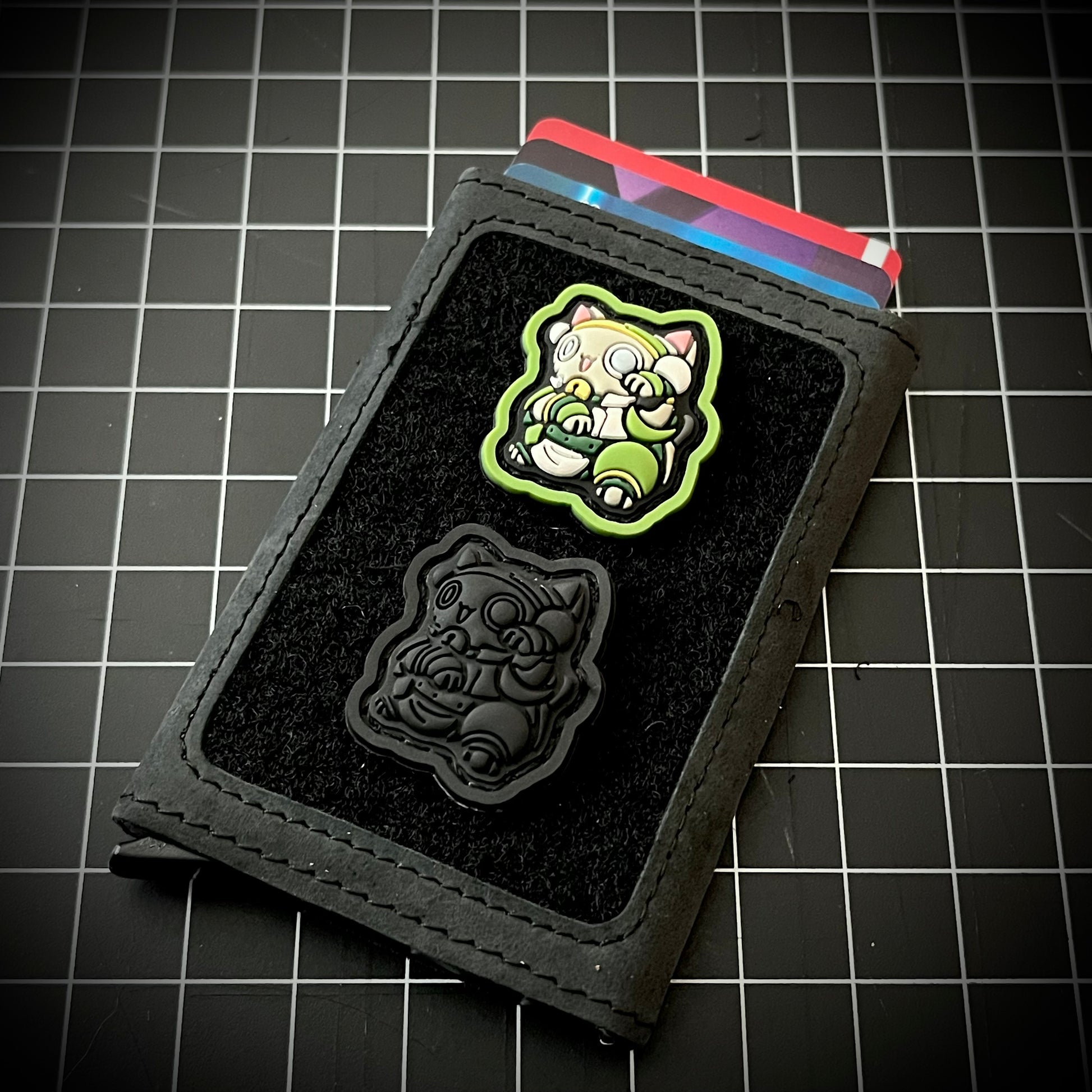Blind Warrior Neko RE and Neko Blackout RE of a cartoon character PVC patch on a velcro wallet with a grid background.