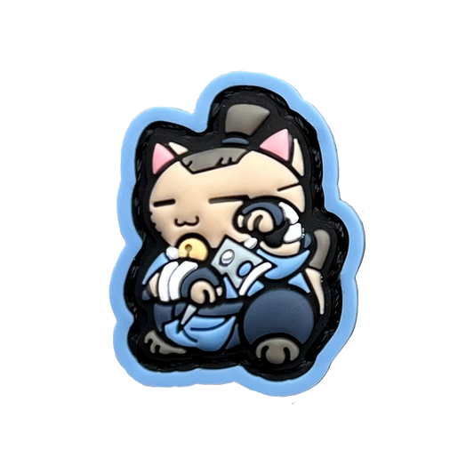 Boomerang Warrior Neko RE PVC ranger eye morale patch of a cartoon character with brown hair wearing blue clothes holding a boomerang sitting in a lucky cat maneki-neko pose.