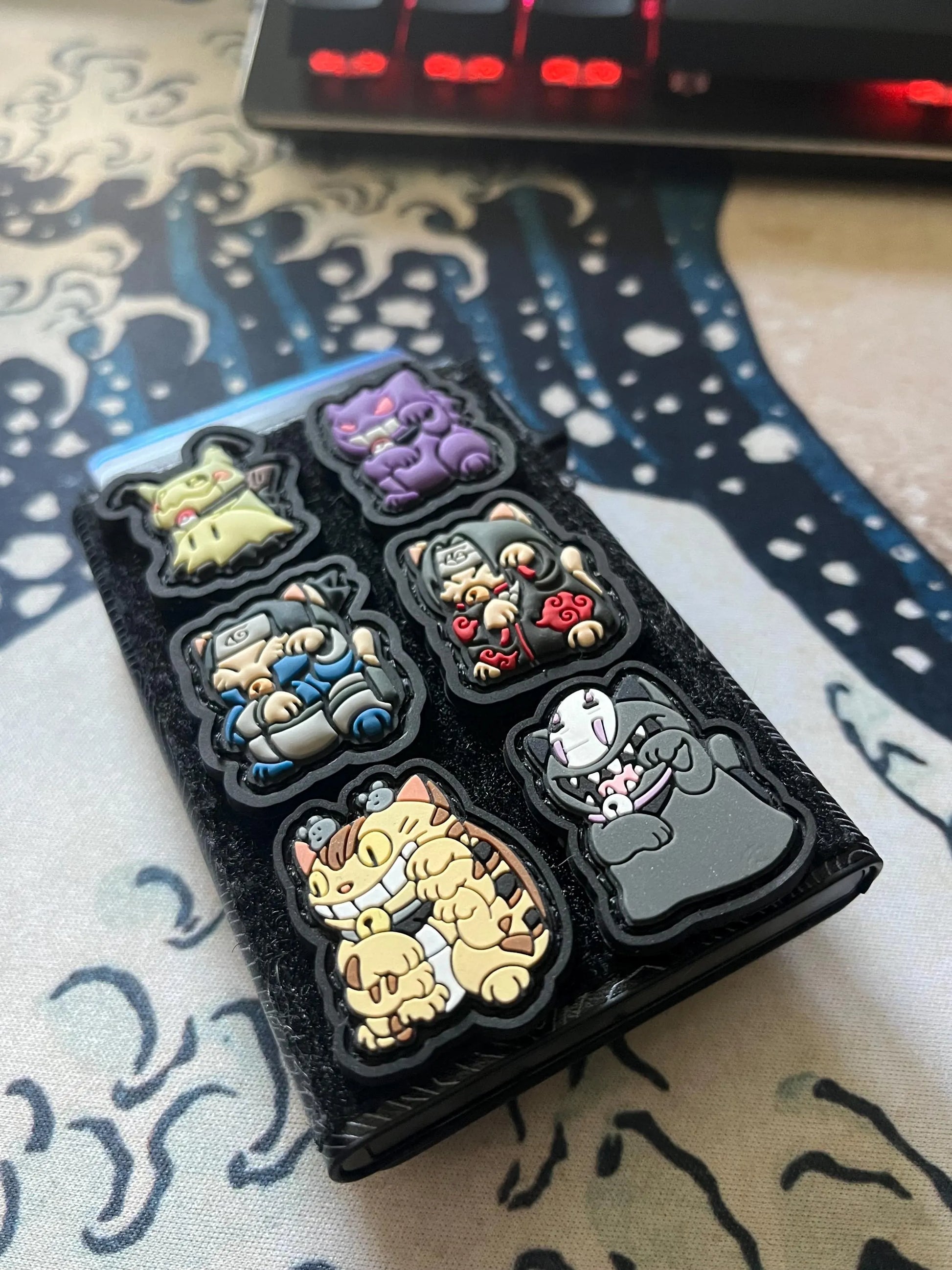 Several colorful Neko patches on wallet with a Great wave background including the Catbus Neko RE patch.