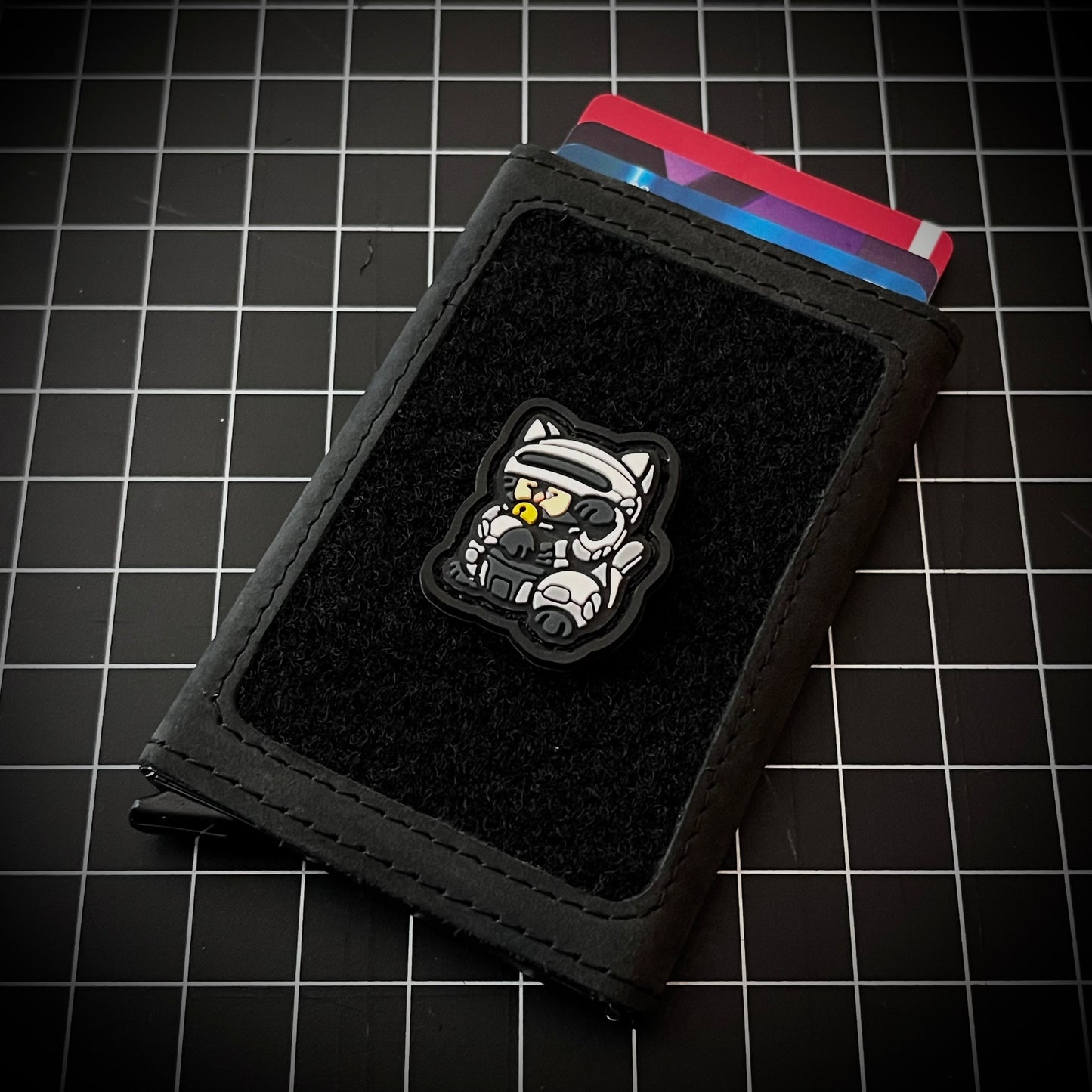 Cyber cop Neko RE PVC ranger eye morale patch of a robotic cartoon character in a lucky cat maneki-neko pose on a velcro wallet and grid background.