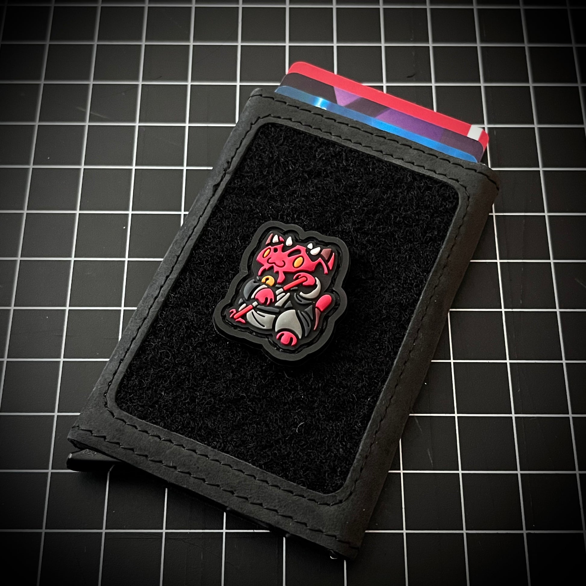 Darth Maul Neko RE PVC ranger eye morale patch of a red cartoon character in a lucky cat maneki-neko pose on a velcro wallet and grid background.