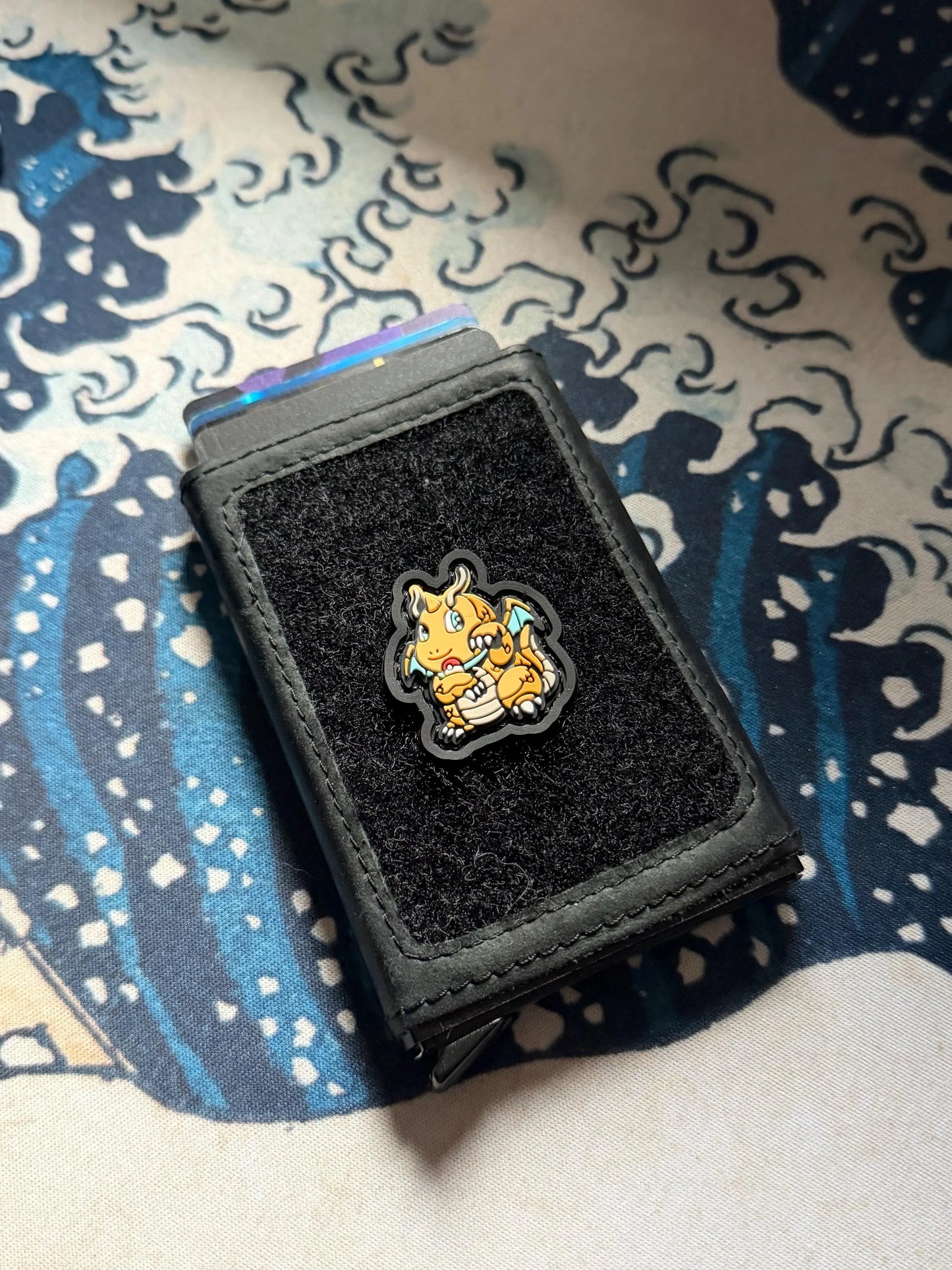 Dragon Monster Neko RE 2D PVC ranger eye patch of an orange dragon in a lucky cat maneki neko pose on a wallet with a Great Wave background.