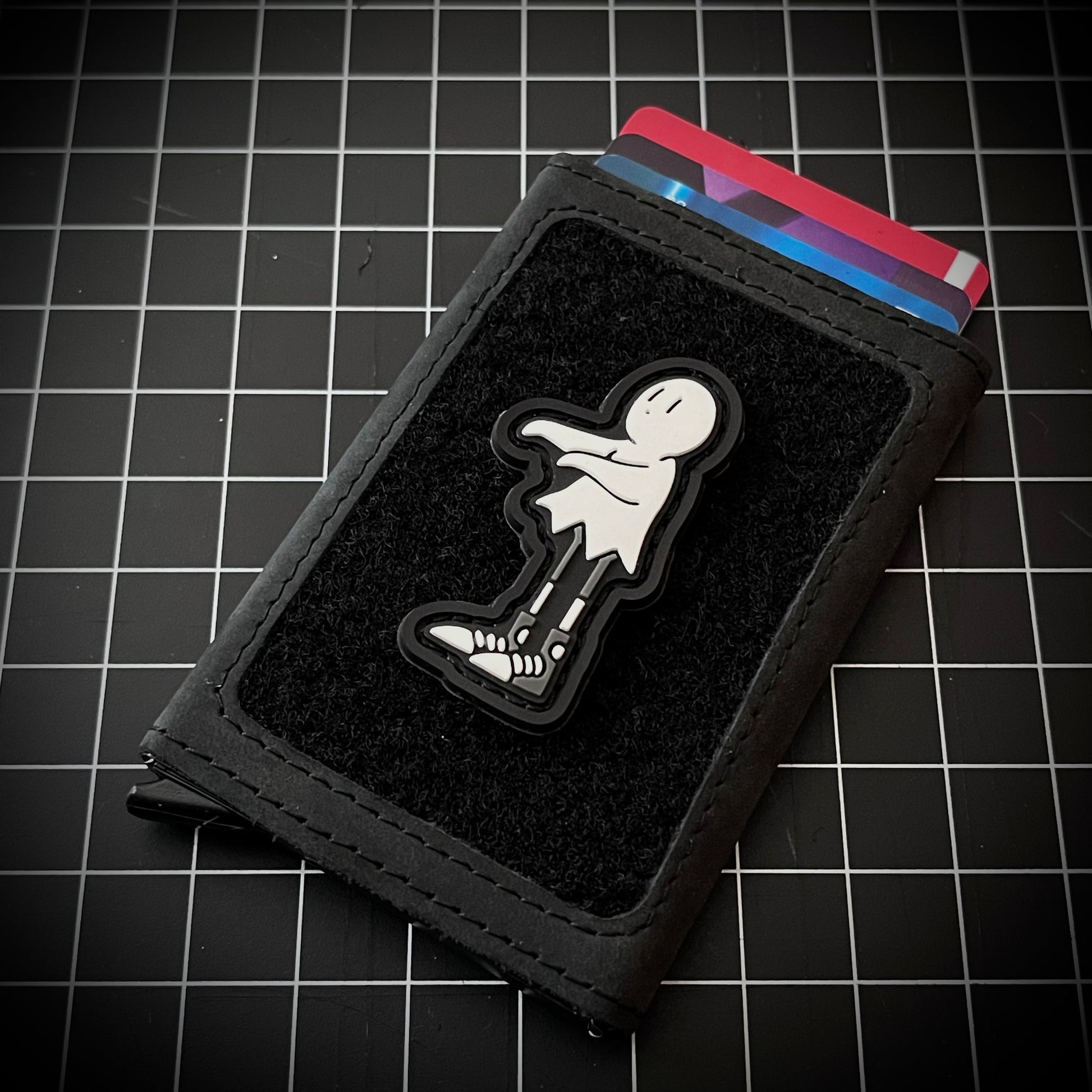  Ghost Guy RE PVC ranger eye morale patch of a white ghost cartoon character with its arms extended facing left on a velcro wallet and grid background.