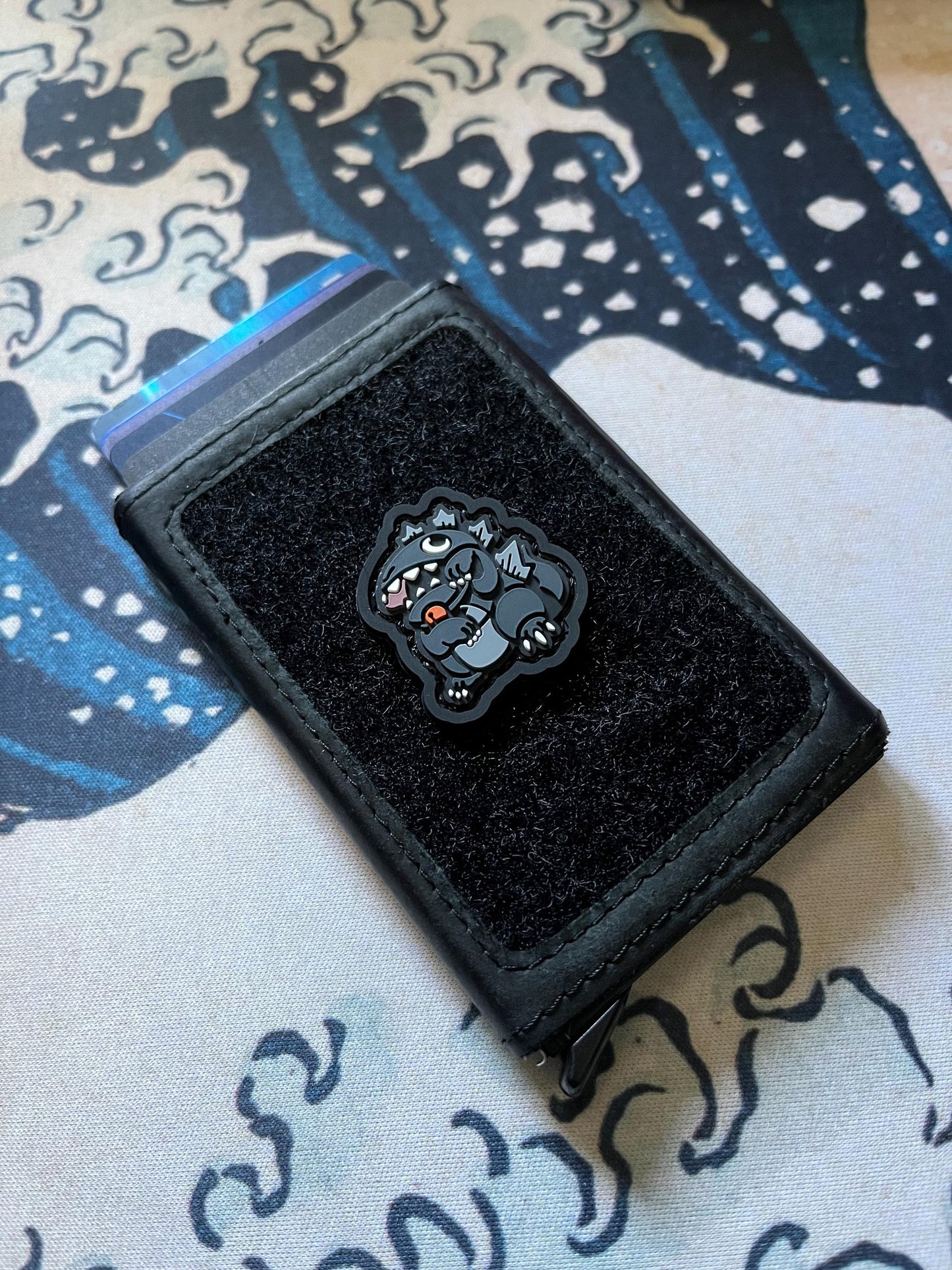 Godzilla Neko RE ranger eye patch showing a kaiju monster in a lucky cat maneko pose on a wallet with a Great Wave background.