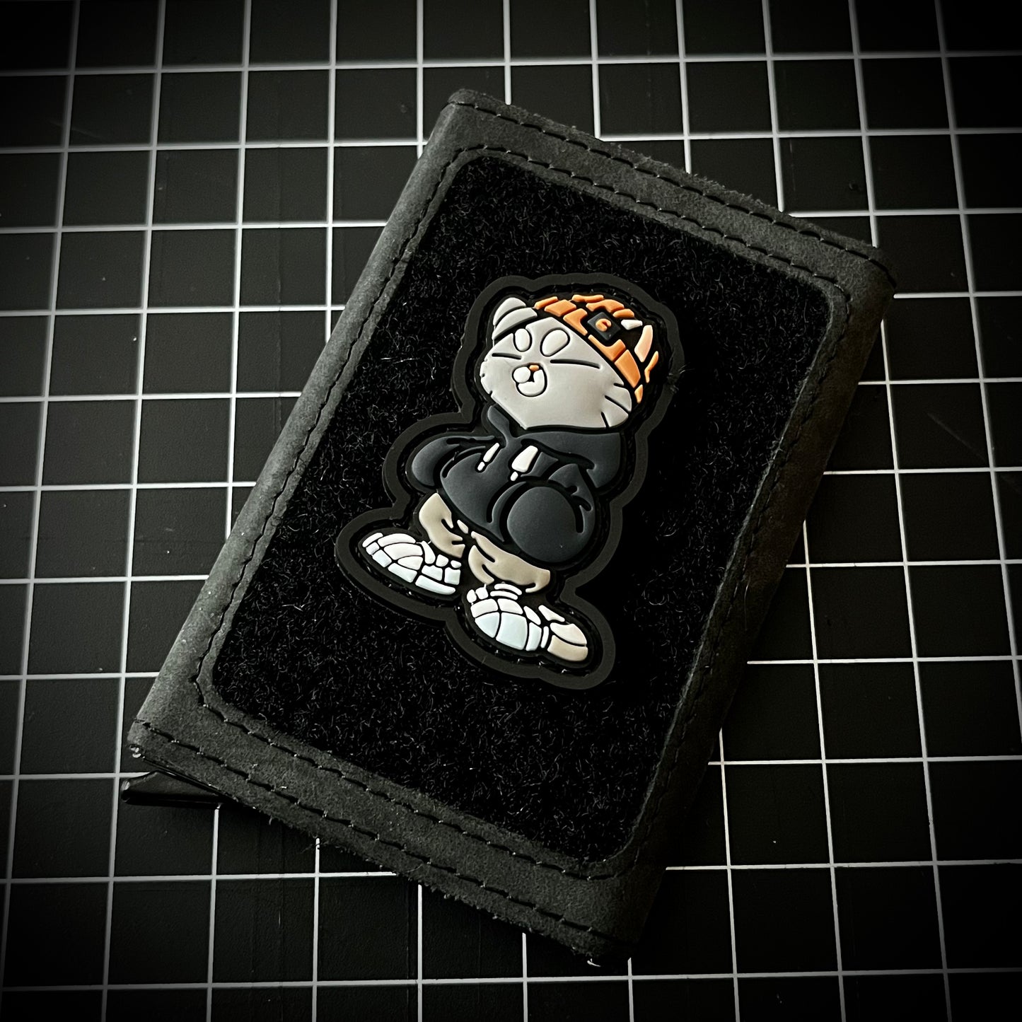 Hoodie Cato Patch PVC ranger eye morale patch of a gray cat in an orange beanie and gray hoodie on a velcro wallet and grid background.