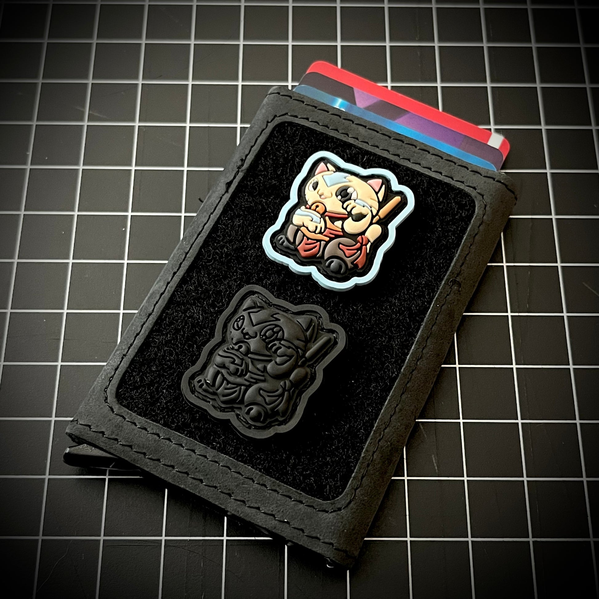 Master of Elements Neko RE and Neko Blackout RE PVC ranger eye patch of a cartoon character in a lucky cat maneki-neko pose on a velcro wallet with a grid background.