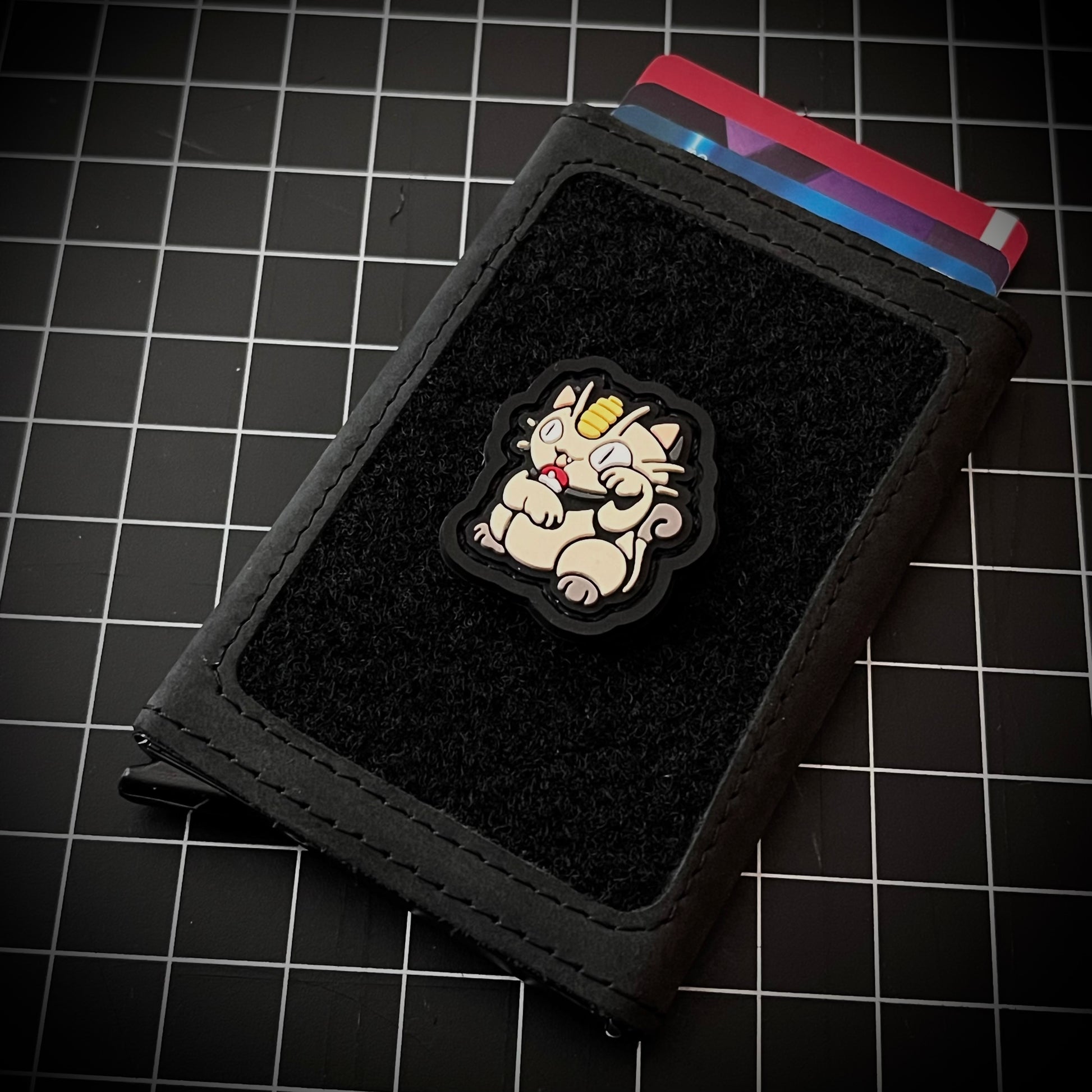 Meowth Neko RE PVC ranger eye morale patch of a white cat with coin forehead sitting in a lucky cat maneki-neko pose on a velcro wallet and grid background.