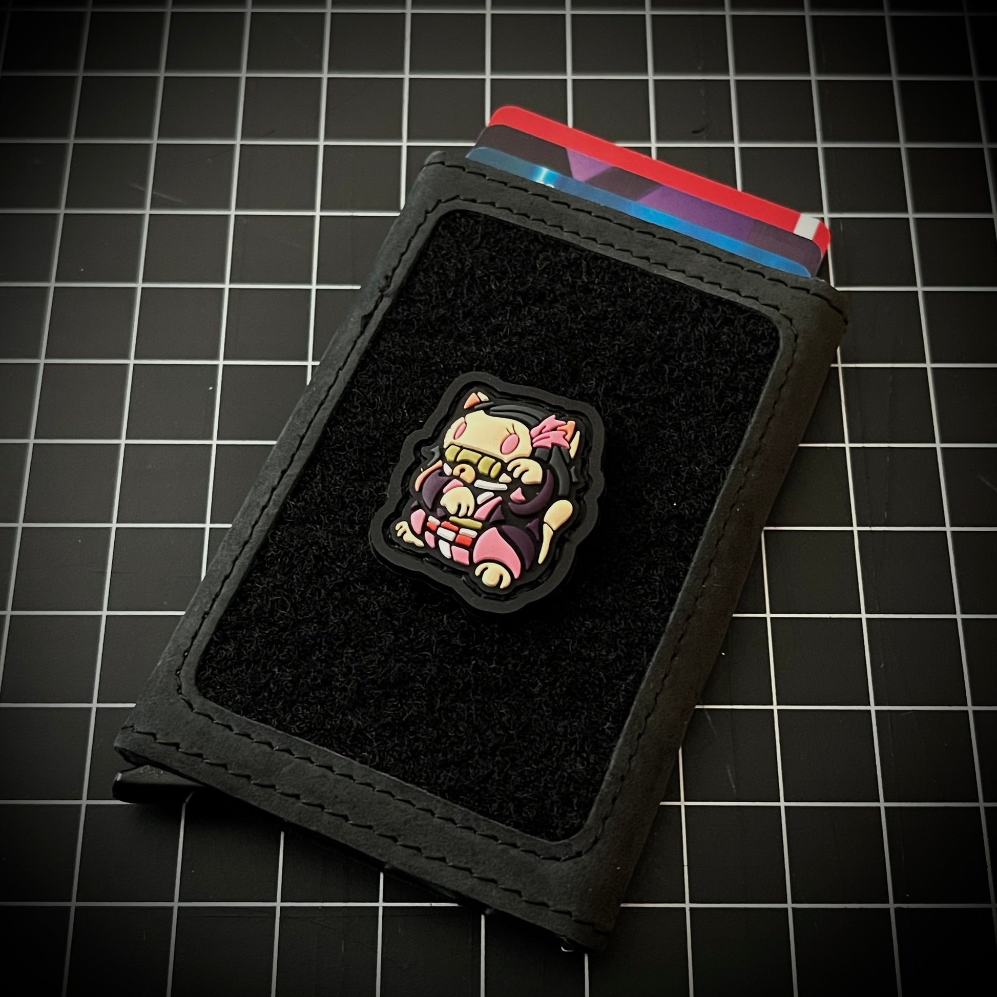 Nezuko Neko RE PVC ranger eye morale patch of nezuko of demon slayer in a lucky cat maneki-neko pose on a velcro wallet and grid background