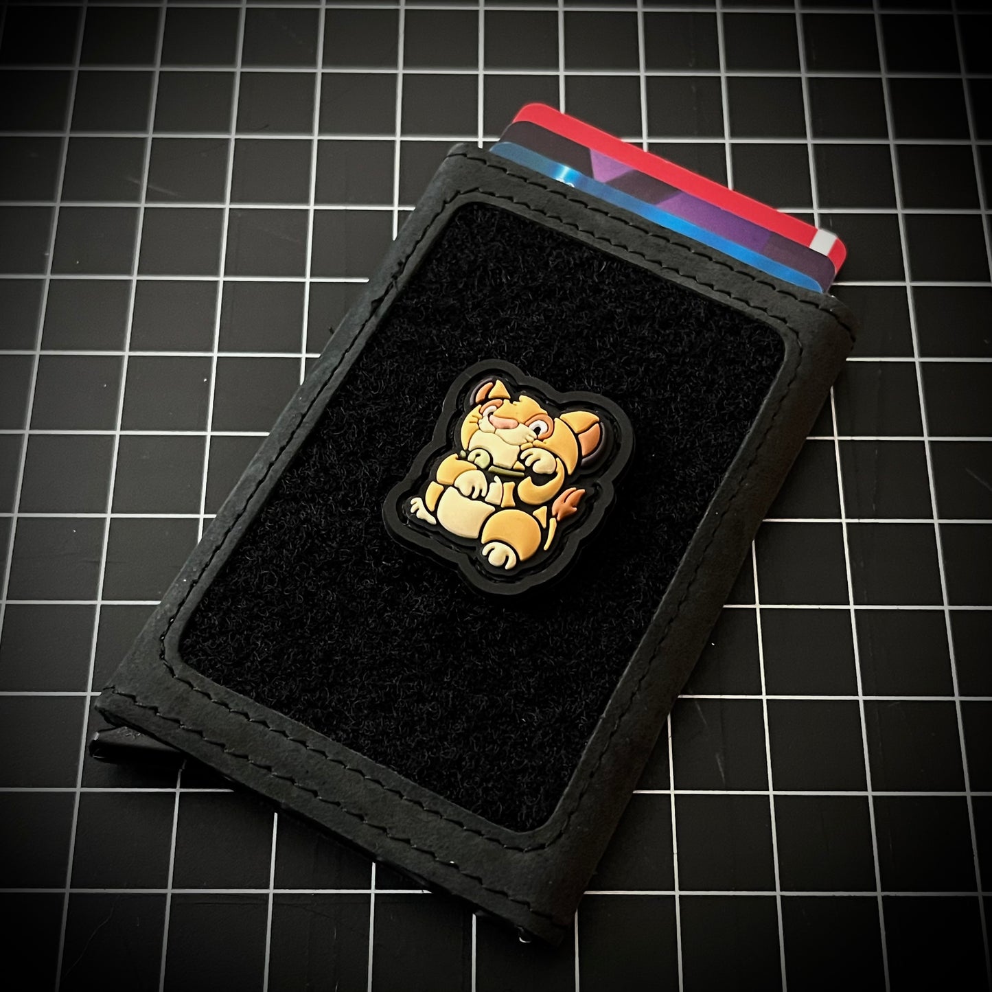 Simba Neko RE PVC ranger eye morale patch of a lion sitting in a lucky cat maneki-neko pose on a velcro wallet with a grid background.