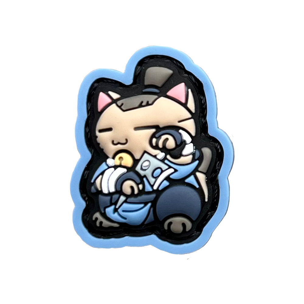 Sokka Neko RE PVC ranger eye morale patch of a cartoon character with brown hair wearing blue clothes holding a boomerang sitting in a lucky cat maneki-neko pose.