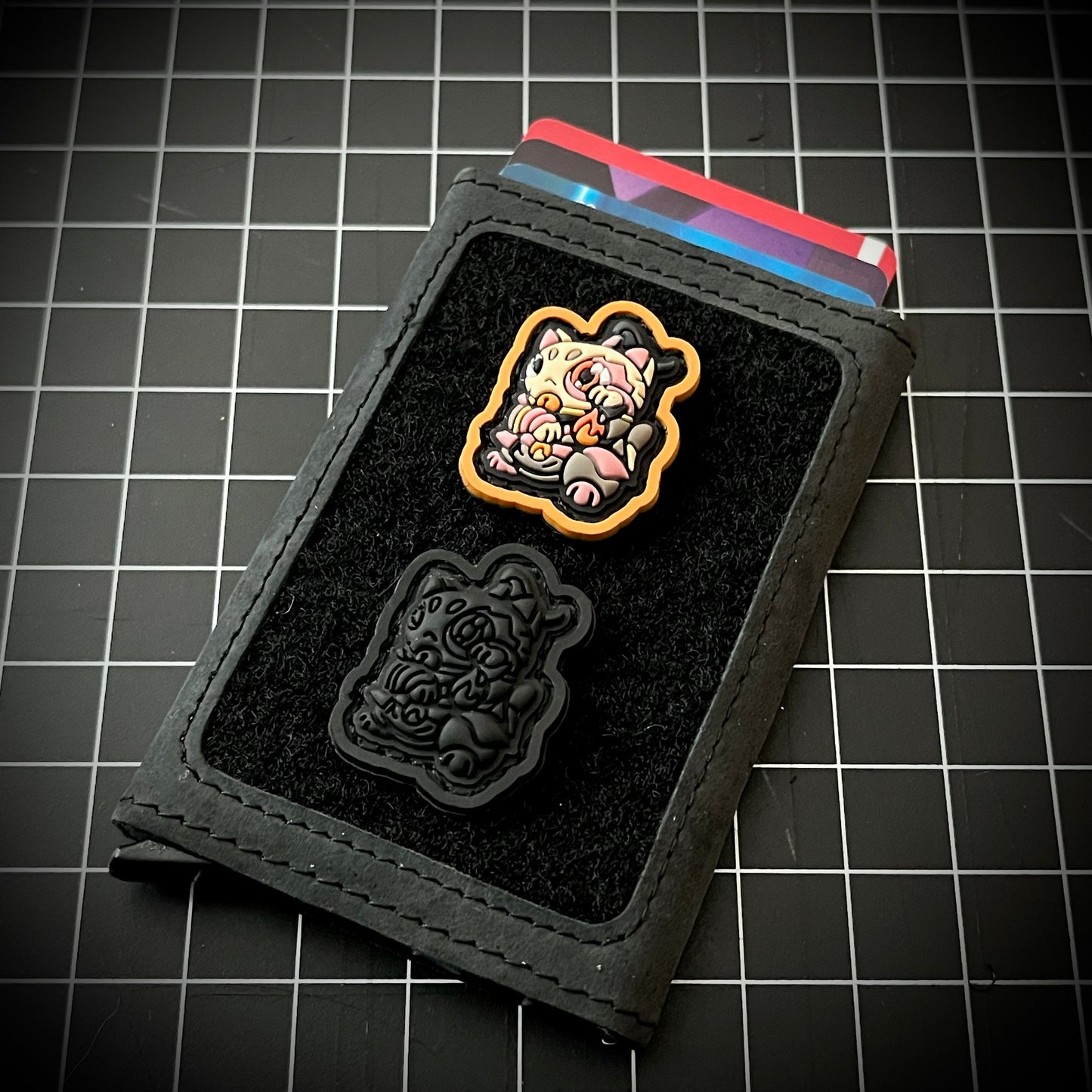 Zuko Neko Blackout RE PVC ranger eye morale patch of a cartoon character fully blacked out in a lucky cat maneko pose on a wallet with a grid background.